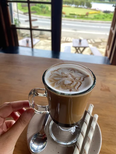 A latte in a glass mug on a wooden table by the window